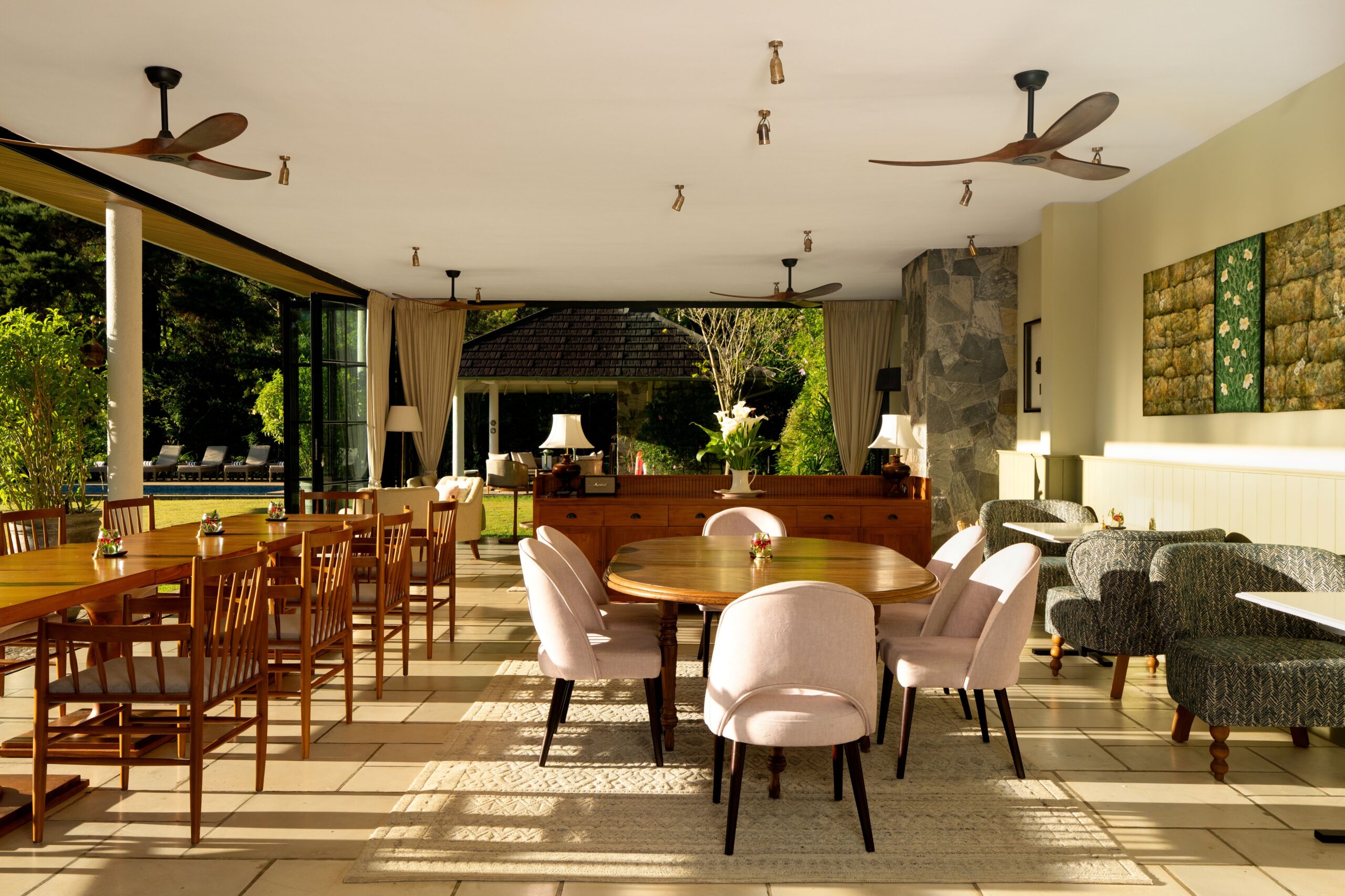 The dining pavilion with round tables, pink chairs and ceiling fans, open to the garden